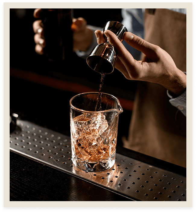 Bartender pouring drink into ice-filled glass.